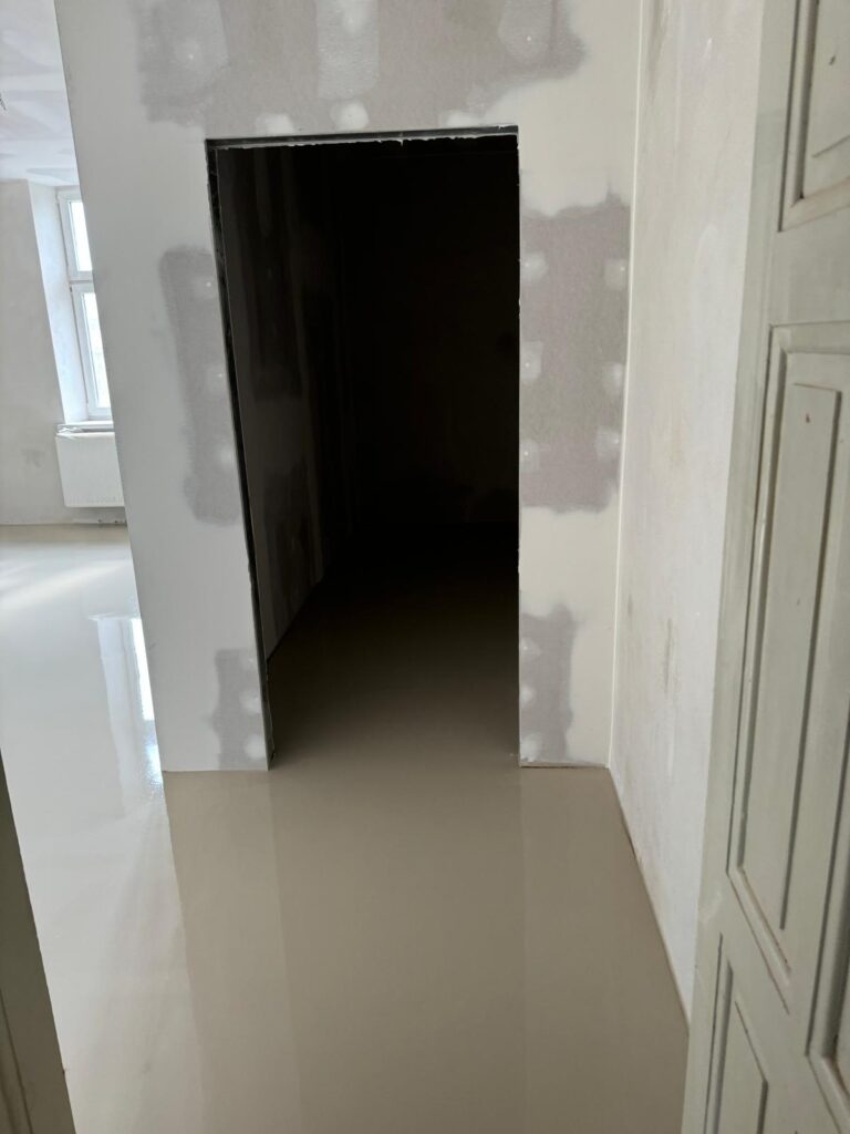 Dokončená nivelace podlahy v rekonstruované místnosti, odrazy oken na hladkém povrchu.