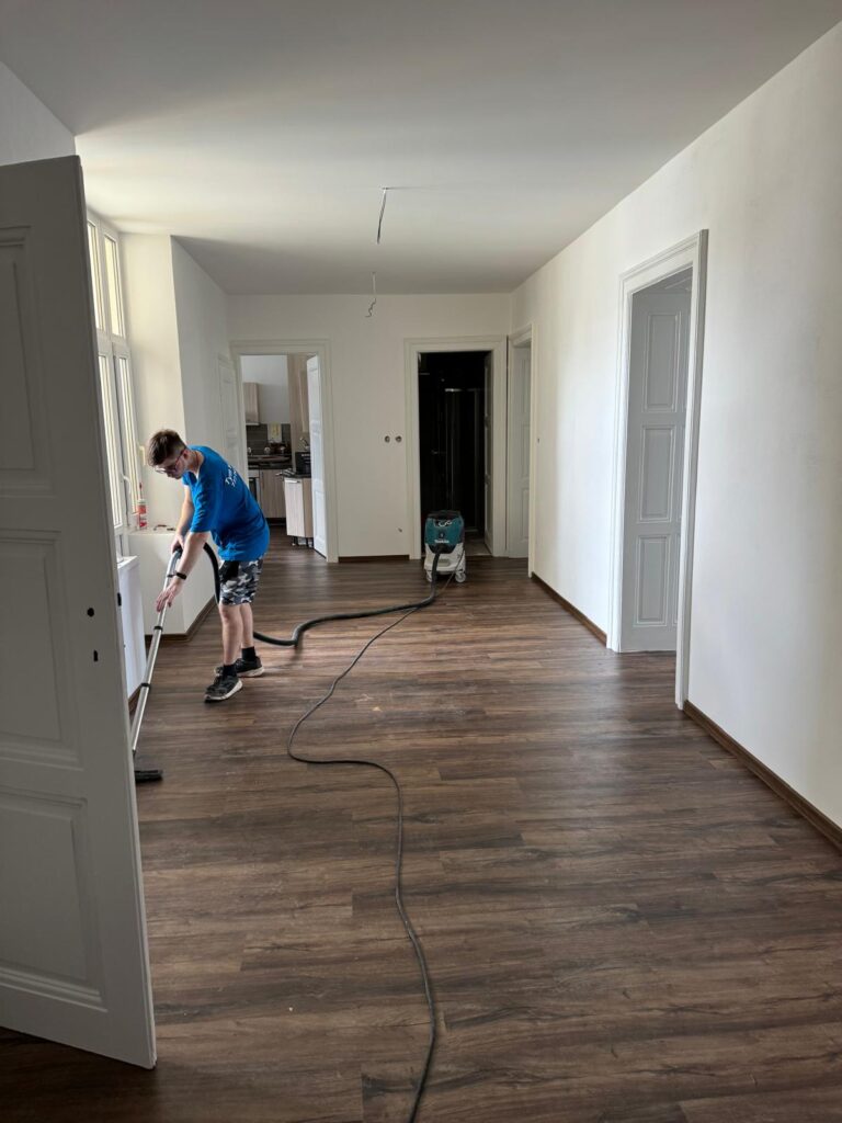 Úklid po dokončení rekonstrukce, pracovník čistí chodbu s novou vinylovou podlahou.