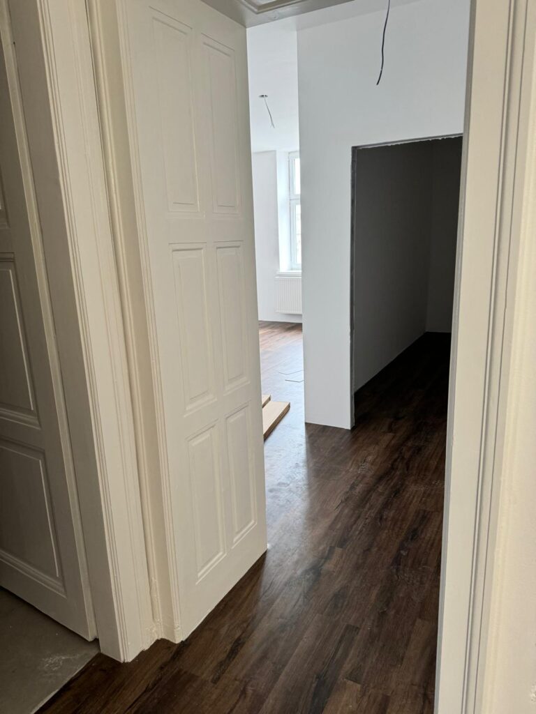 Chodba s novou vinylovou podlahou v tmavém dekoru dřeva, přechod do obytné místnosti.