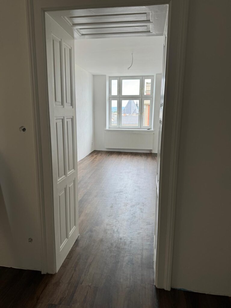 Zrekonstruovaný pokoj s novou vinylovou podlahou v dekoru tmavého dřeva a čistě bílými stěnami.