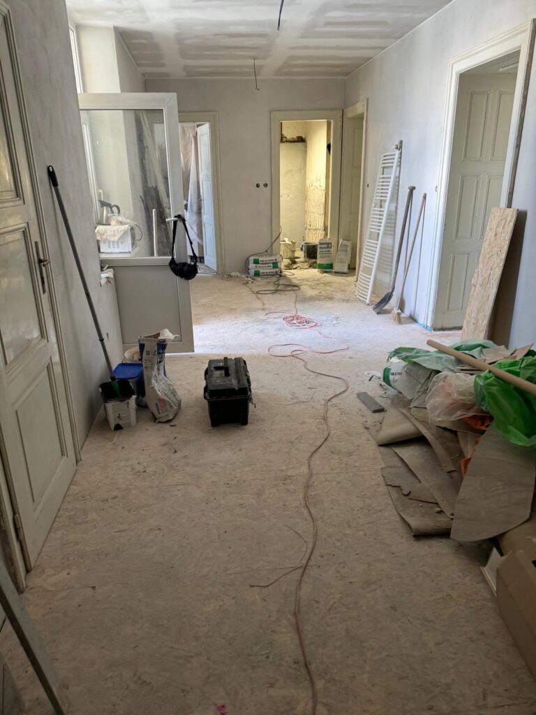 Pohled na rekonstruovanou chodbu s OSB deskami na podlaze, nářadí a materiál připravený na další práce.