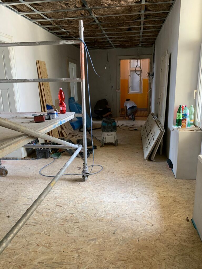 Rekonstrukční práce na stropní konstrukci a pokládce podlahy z OSB desek, místnost připravená pro další stavební fáze.